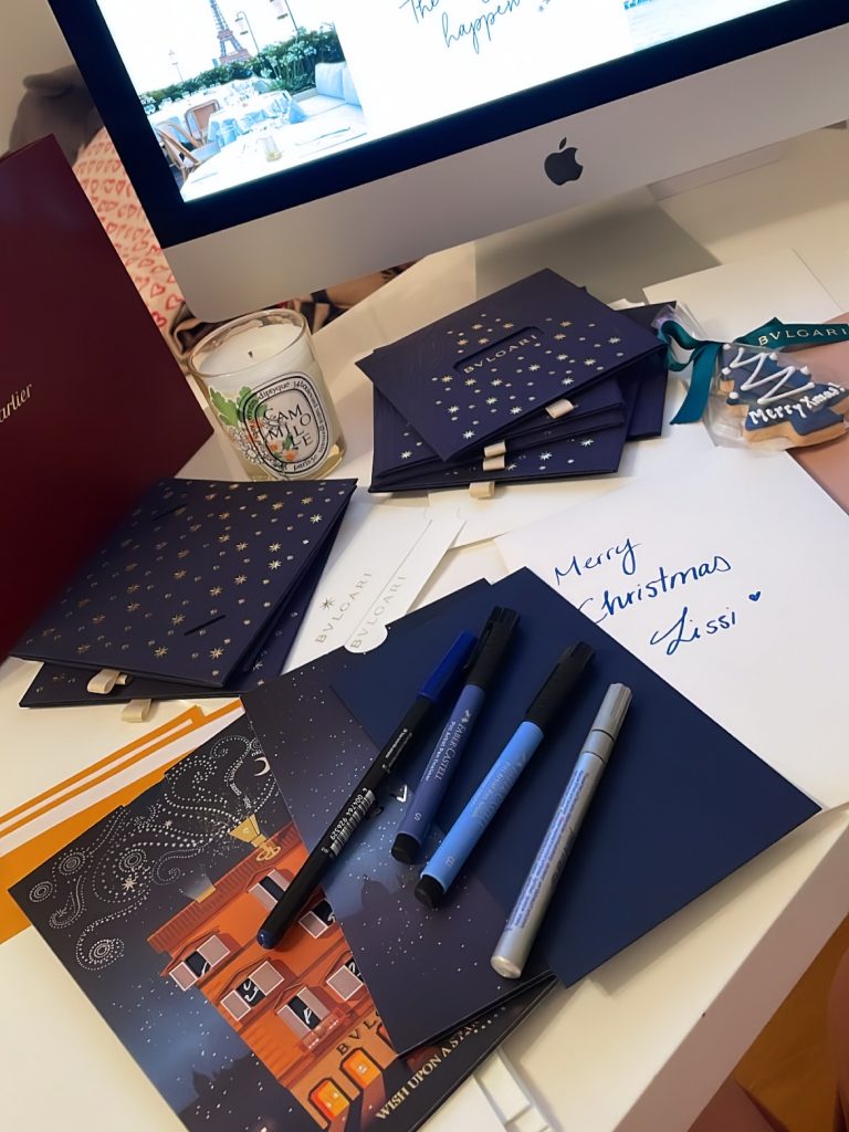 Writing Christmas cards at a candlelit desk, a calming winter self-care ritual that brings joy and connection. | THE DAILY HAPPINESS