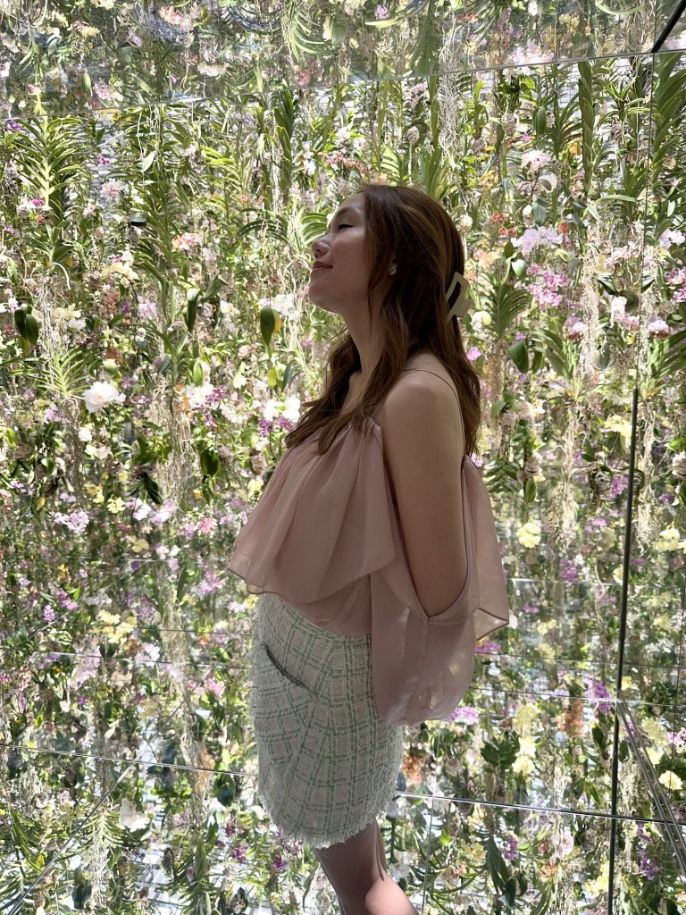 Standing among flowers in a calm installation, representing presence, beauty, and starting with intention.